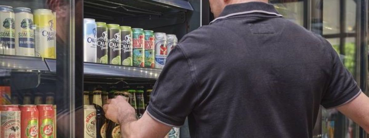 Un client d'une boutique de station-service choisit dans le rayon une bière.
